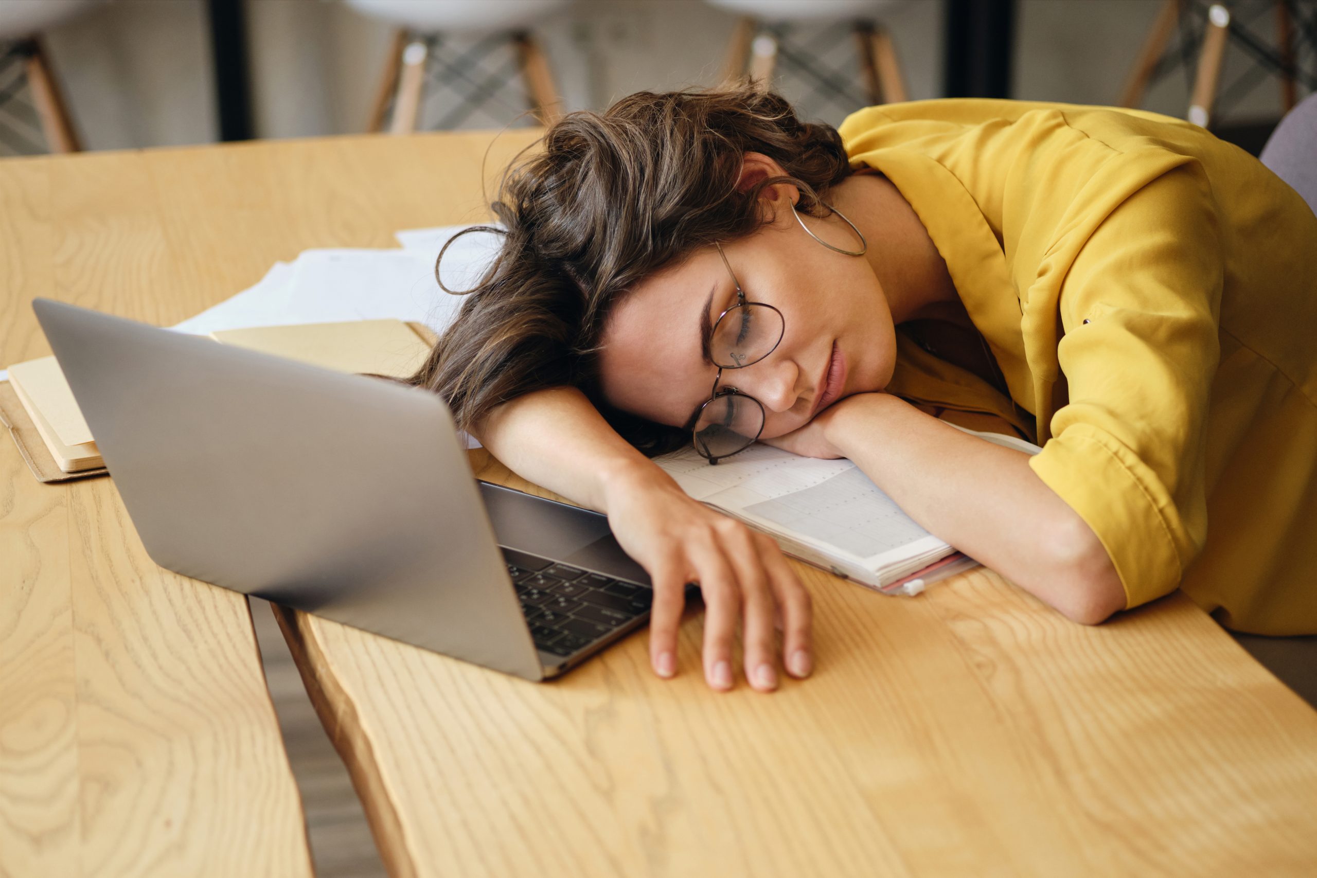 Young tired woman in eyeglasses asleep on desk with laptop and d