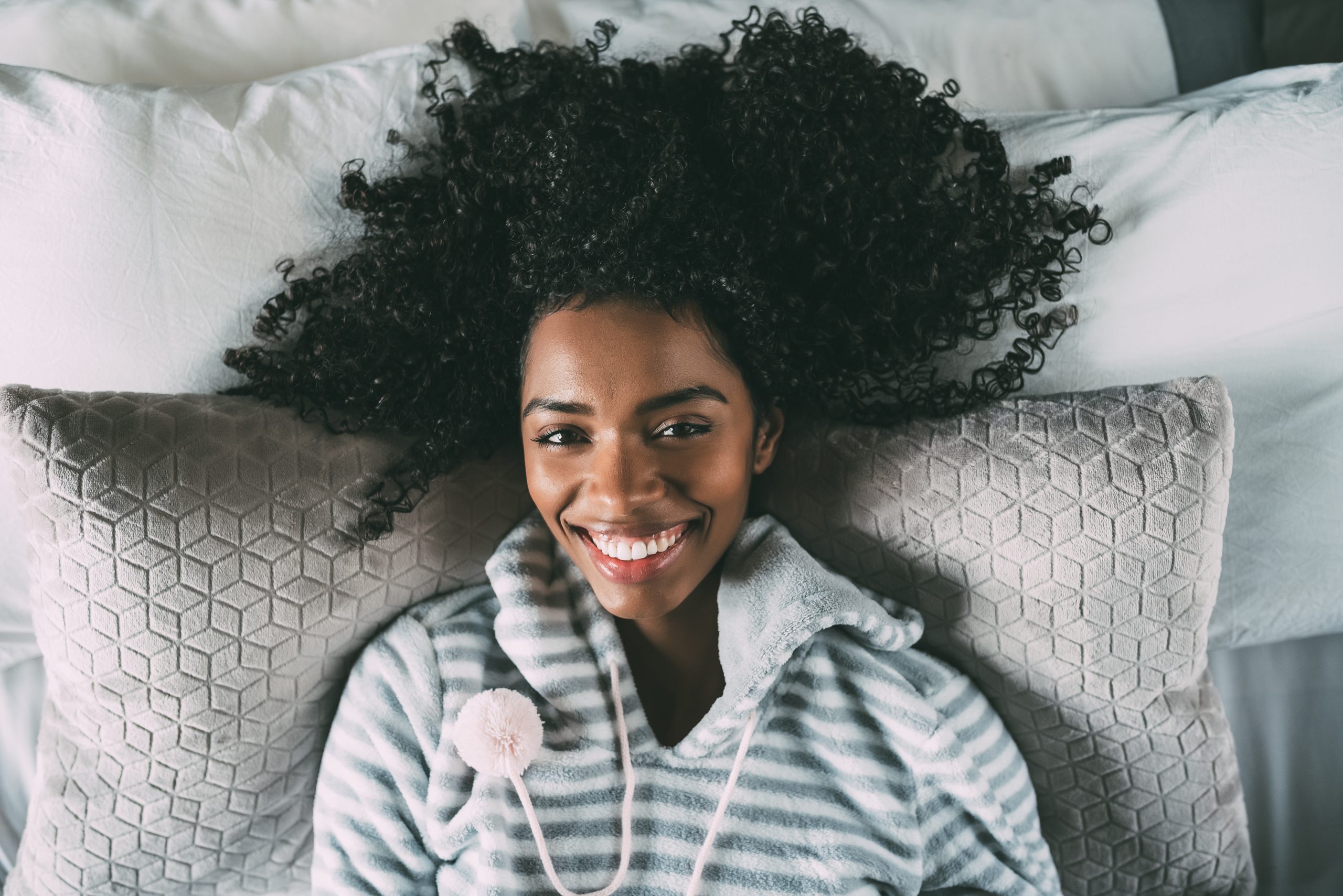 Beautiful black woman with curly hair smiling and lying on bed looking at the camera