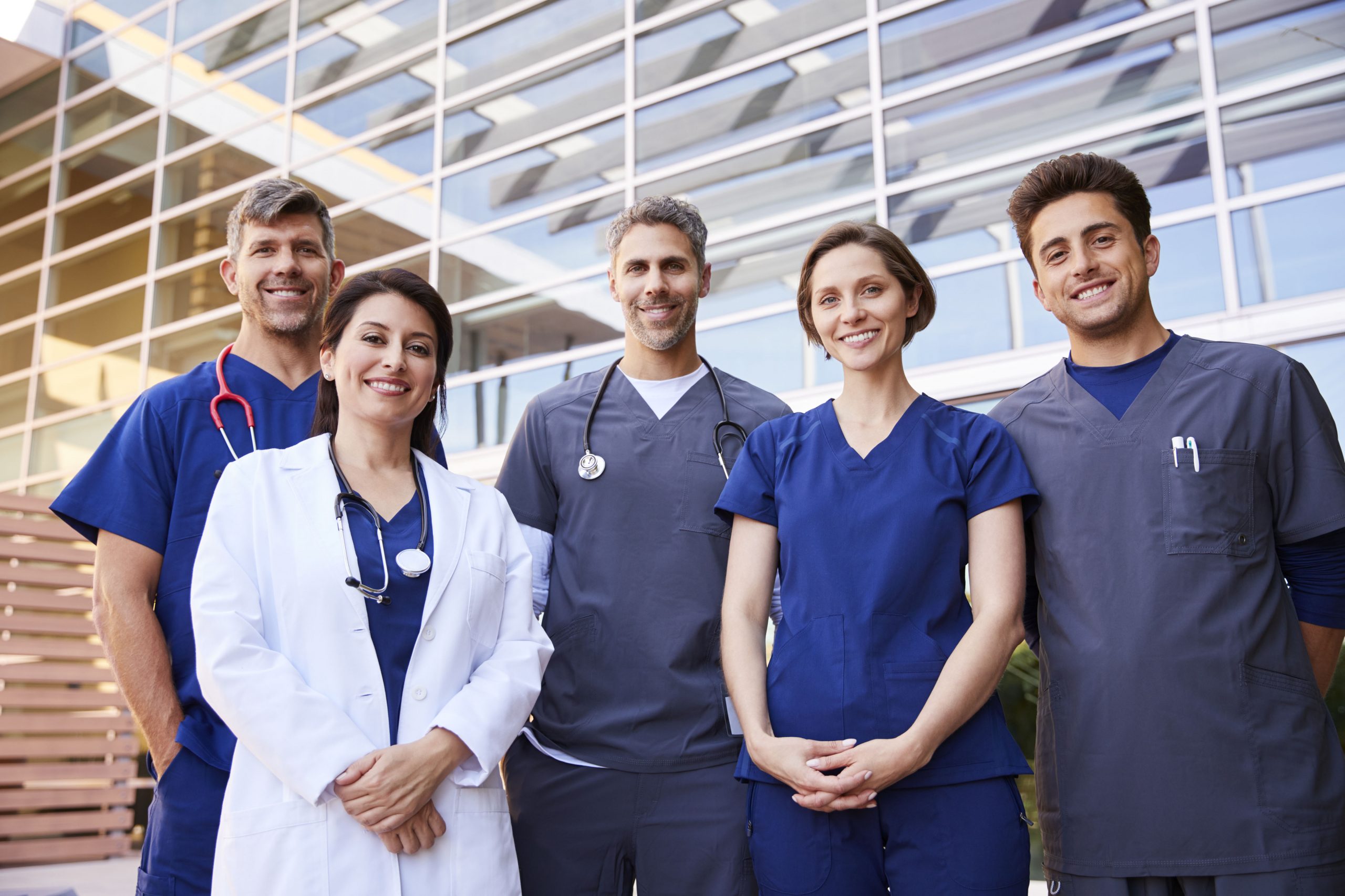 Five healthcare colleagues standing outdoors, group portrait