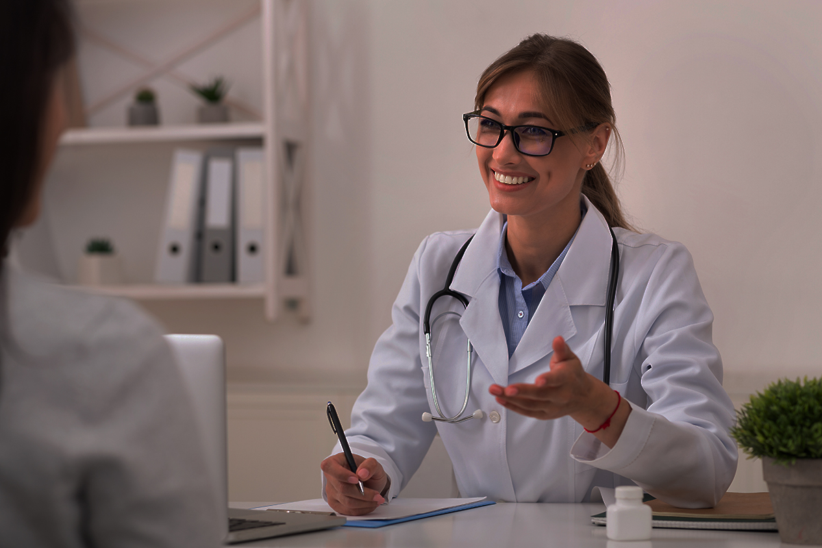 Smiling Doctor Woman Talking With Unrecognizable Patient Sitting In Office