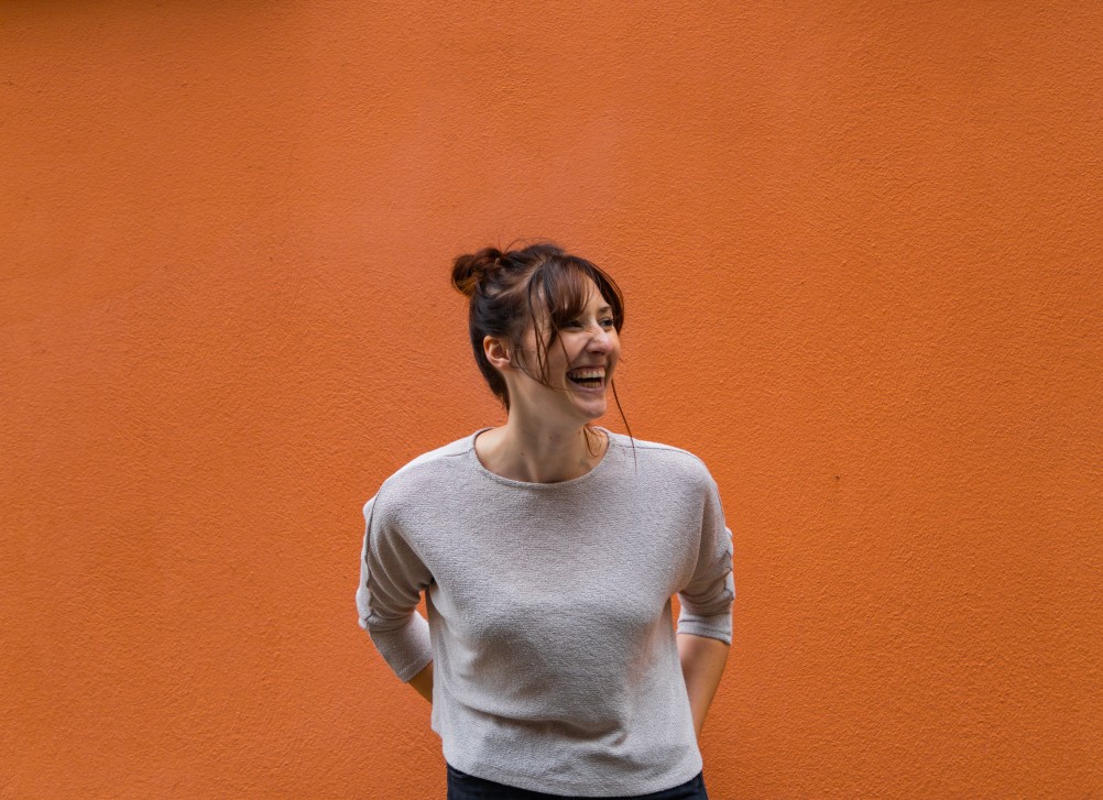young-woman-laughing-and-smiling-in-front-of-an-orange-wall_t20_oRWkRQ